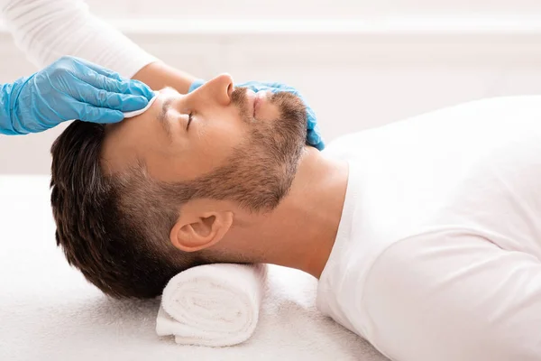 Kosmetolog čištění vousatý muž tvář s tonerem před léčbou — Stock fotografie