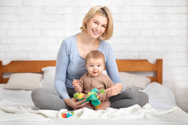 Mère jouant avec son enfant, assise sur le lit — Photo