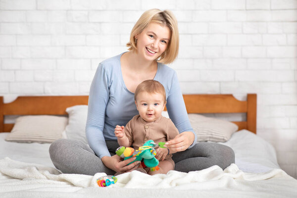 Mother playing with her infant child, sitting on bed