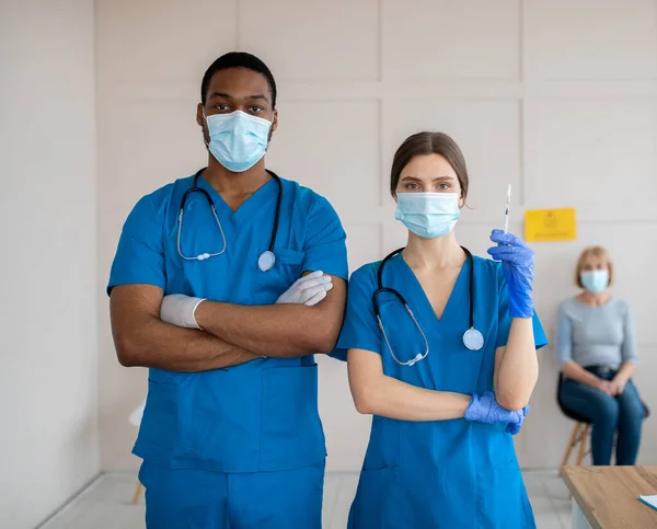 Portrait of doctors in medical masks and uniforms holding syringe with covid-19 vaccine at health centre — Stock Photo, Image