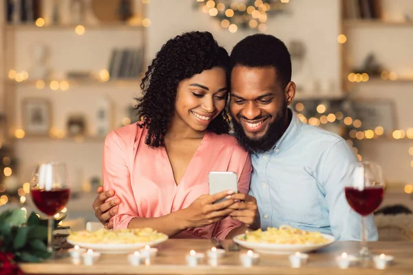 Smiling black man and woman using smartphone during dinner — Stock Photo, Image