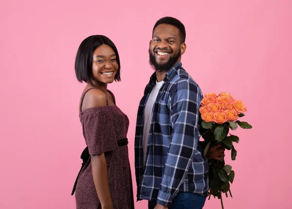Smiling black couple with bunch of flowers smiling and looking at camera, celebrating Valentines Day on pink background — Stock Photo, Image