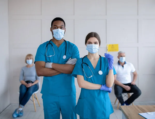 Male and female doctors wearing uniforms and face masks, holding syringe with coronavirus vaccine at clinic — Stock Photo, Image