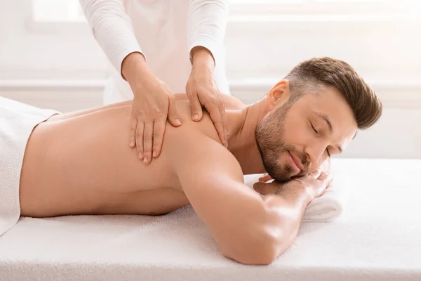 Terapeuta feminino esfregando alegre homem ombros no salão de spa — Fotografia de Stock