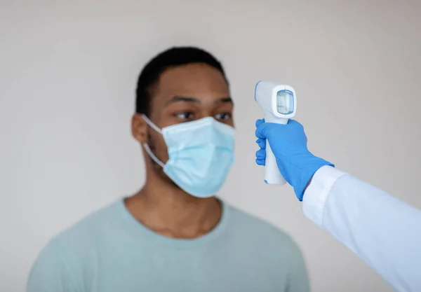 Doctor measuring black mans temperature with electronic thermometer before covid-19 vaccination at clinic