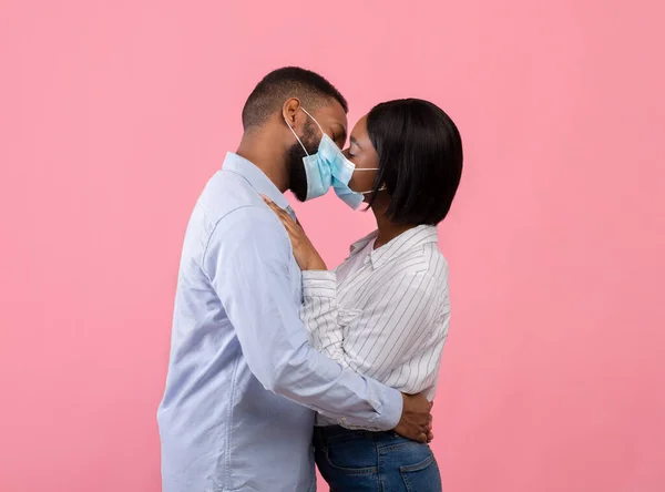 Celebrando el Día de San Valentín durante la epidemia de coronavirus. Pareja negra en máscaras faciales besándose sobre fondo rosa —  Fotos de Stock