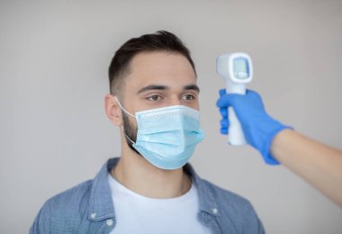 Doktor, klinikte koronavirüs aşısı olmadan önce genç adamın sıcaklığını dijital termometreyle ölçüyor.