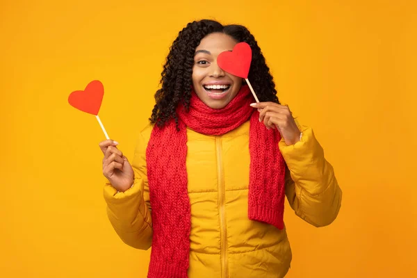 Mulher negra posando com corações de papel que cobrem o olho, fundo amarelo — Fotografia de Stock