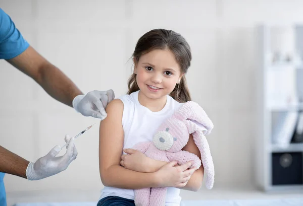 Bonne petite fille avec lapin jouet se faire injecter le vaccin contre le coronavirus à l'hôpital. Soins de santé et concept médical — Photo