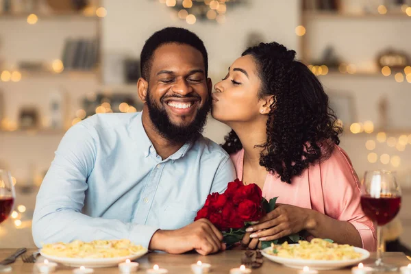 Jovem mulher negra beijando seu homem segurando flores — Fotografia de Stock