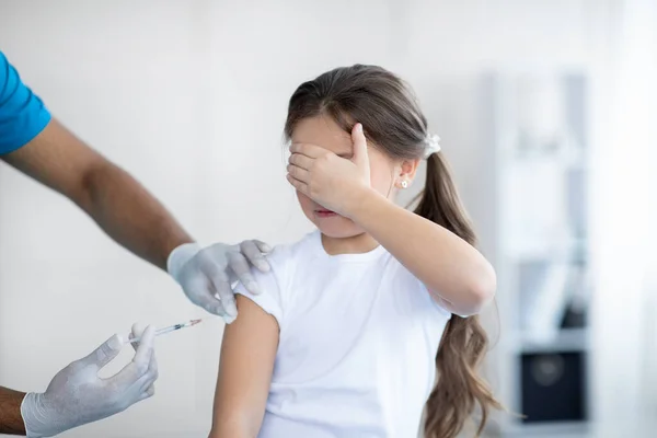 Bang klein meisje dat covid-19 vaccin krijgt, dat haar ogen bedekt in angst voor injectie in de kliniek — Stockfoto