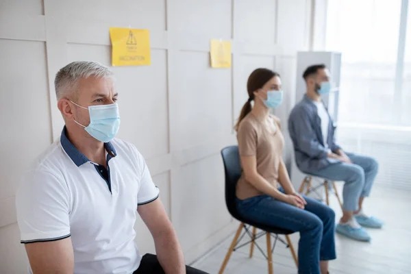 Covid-19 vaccination. Senior man in mask waiting to receive coronavirus vaccine injection, sitting in queue at clinic — Stock Photo, Image