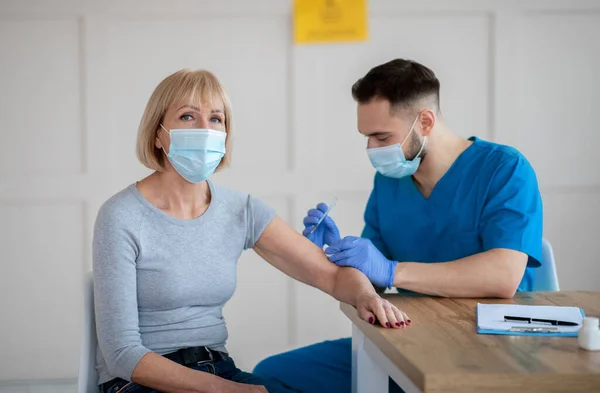 Senior Caucasian woman receiving intramuscular injection of coronavirus vaccine during doctors appointment at clinic — Stock Photo, Image