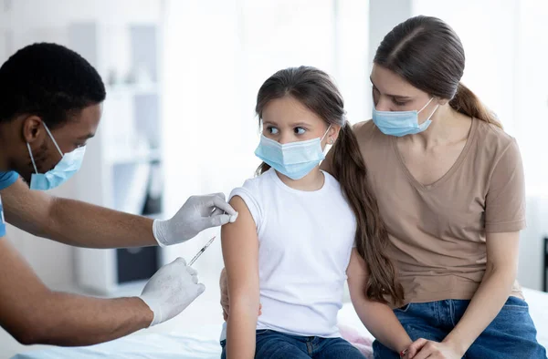 Moeder en dochter met medische maskers die worden gevaccineerd tegen covid-19, arts die het coronavirusvaccin injecteert — Stockfoto