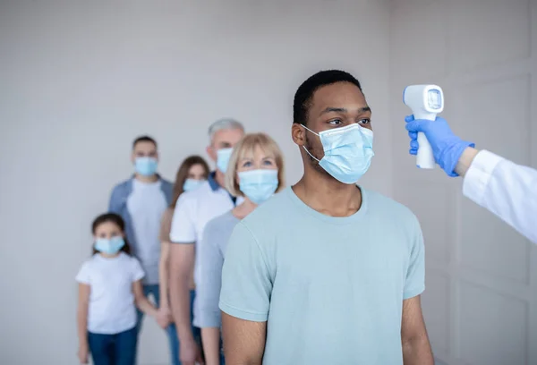 Black man in face mask standing in line at clinic, doctor measuring his temperature before covid-19 vaccination — Stock Photo, Image