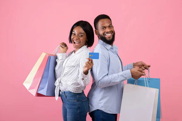 Portret van een zwart koppel met cadeauzakjes en creditcard, winkelen voor Valentijnscadeaus op afstand op roze achtergrond — Stockfoto