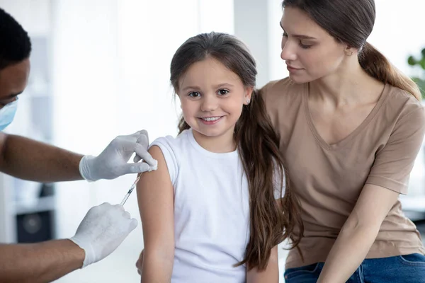 Linda chica feliz visitando al médico con su madre, recibiendo la inyección de la vacuna covid-19 en el hospital — Foto de Stock
