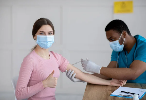 Mujer joven recibiendo la inyección de la vacuna covid-19, mostrando el gesto pulgar hacia arriba, recomendando la inmunización contra el coromavirus — Foto de Stock