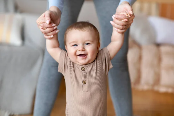 Bébé heureux faisant les premiers pas avec l'aide de la mère, intérieur de la maison — Photo