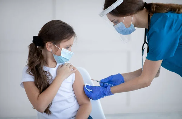 Vacunación con Covid-19. Niña con máscara protectora que recibe la inyección de la vacuna contra el coronavirus del médico en la clínica — Foto de Stock