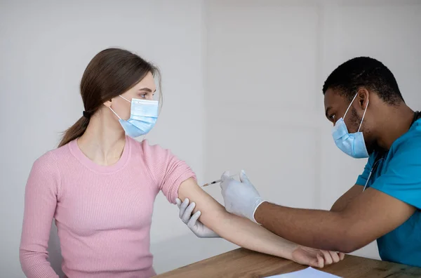 Black doctor making covid-19 vaccine injection to female patient at clinic. Medical treatment against global pandemic — Stock Photo, Image