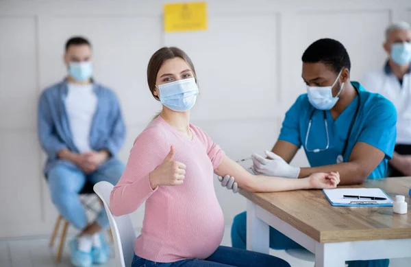 Mujer embarazada que recibe la inyección de la vacuna contra el coronavirus en la clínica, mostrando un gesto pulgar hacia arriba, recomendando la inmunización — Foto de Stock