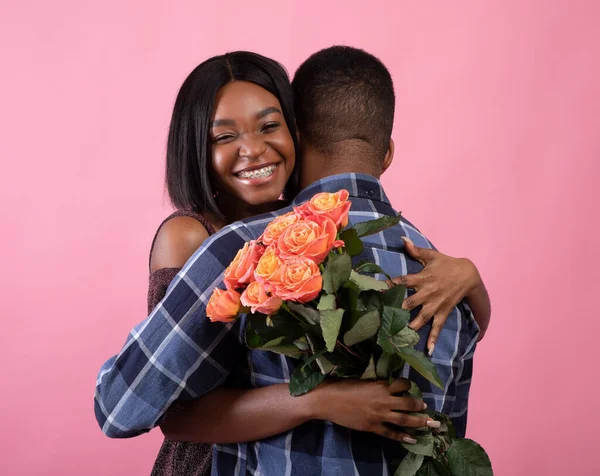 Счастливая черная леди обнимает своего парня, держит букет роз, празднует День Святого Валентина на розовом фоне — стоковое фото