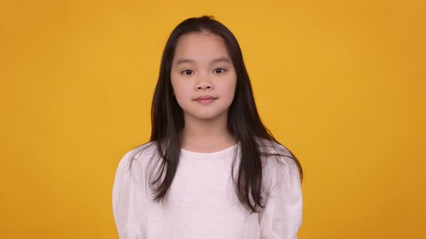 Studio πορτρέτο του χαριτωμένο κορίτσι της Ασίας, κοιτάζοντας κάμερα, πορτοκαλί φόντο — Αρχείο Βίντεο