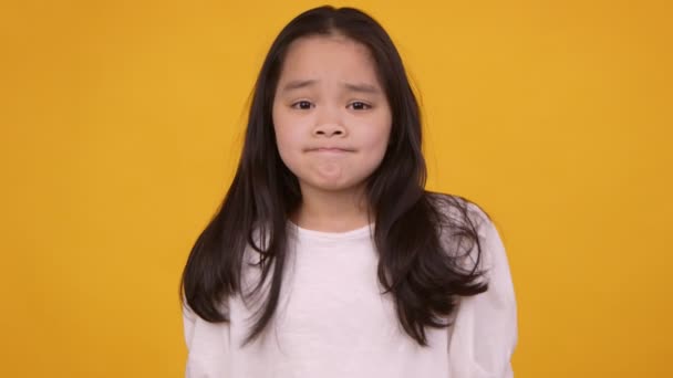 Schattig oosters meisje schouders ophalen en het verspreiden van handen, gevoel onzeker en twijfelachtig, oranje studio achtergrond — Stockvideo