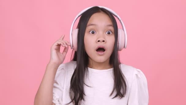 Emocionado chica asiática en auriculares inalámbricos disfrutando de la música y el baile, rosa fondo del estudio — Vídeos de Stock