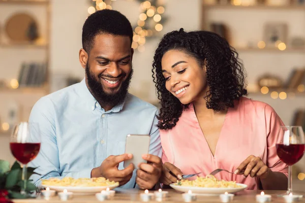 Улыбающаяся черная пара с помощью смартфона во время романтического ужина — стоковое фото