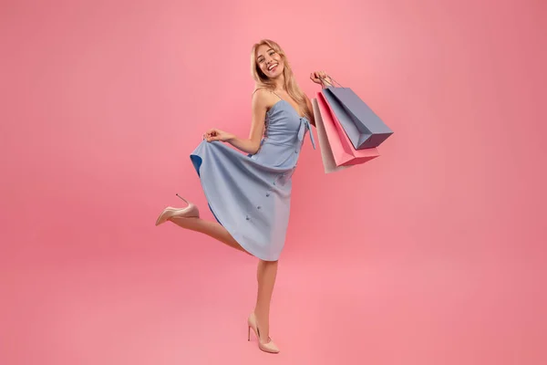 Портрет повної довжини молодої леді з сумками відчуває себе щасливим, купуючи подарунки на свято на рожевому тлі — стокове фото