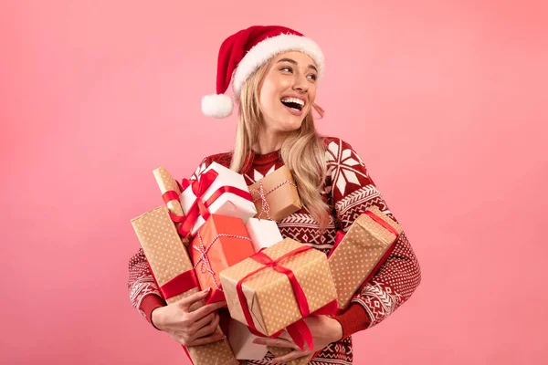 Mooie blanke vrouw in kerstoutfit met stapel gewikkelde kerstcadeaus op roze achtergrond. Vakantie verkoop — Stockfoto