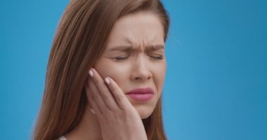 Diş ağrısından muzdarip genç bir kadının portresini yakından çek, ağrıyan çenesine, mavi stüdyo geçmişine dokun