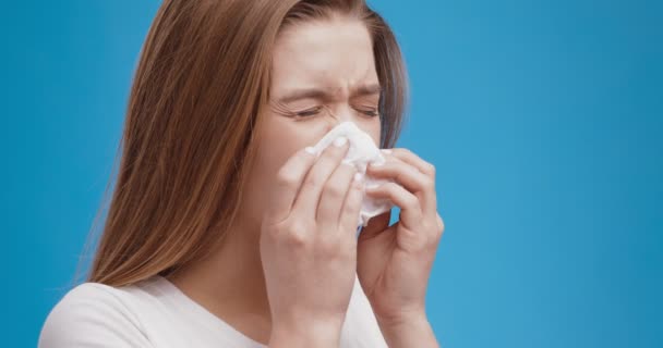 Problema de alergia. Retrato de jovem senhora espirros, soprando nariz com tecido, fundo estúdio azul, câmera lenta — Vídeo de Stock