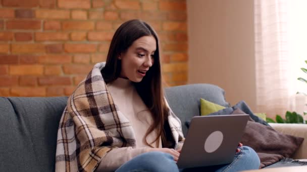 Ενθουσιασμένη νεαρή μοναχική γυναίκα διαβάζει email στο laptop, κάθεται στον καναπέ στο σπίτι, αργή κίνηση — Αρχείο Βίντεο