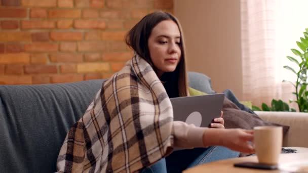 Молодая женщина работает на ноутбуке дома, пьет кофе и наслаждается хорошими новостями на экране компьютера, замедленной съемки — стоковое видео