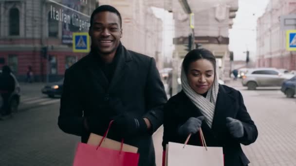 Gelukkig Afrikaans Amerikaans paar met shopper tassen dansen buiten, plezier hebben in de buurt van winkelcentrum gebouw, slow motion — Stockvideo