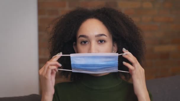 Joven mujer afroamericana poniéndose máscara médica protectora antes de salir, primer plano retrato, cámara lenta — Vídeos de Stock