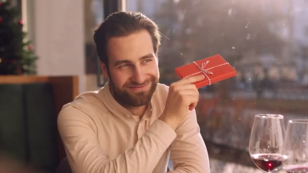 Close up portræt af ung mand viser nuværende kasse til sin kæreste under dato i cafe, slow motion – Stock-video