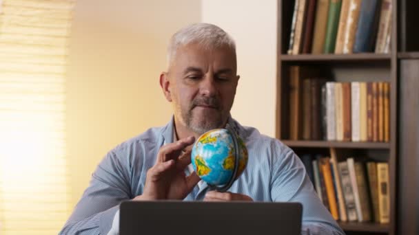 Uomo maturo guardando la mappa del mondo e sognando di vacanza, seduto vicino al computer portatile a casa — Video Stock