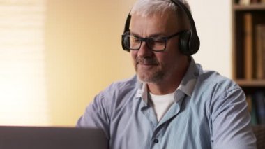 Diz üstü bilgisayarda çalışan ve ofis masasında müzik dinleyen olgun bir adam, yavaş çekim, kapat.