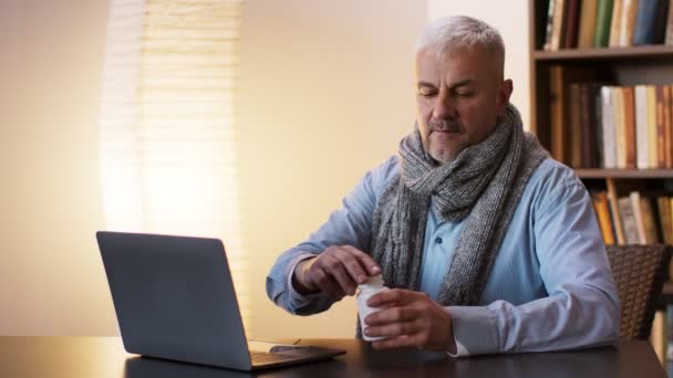 生病的商人，戴着围巾，坐在工作场所，拿着手提电脑，吃药 — 图库视频影像