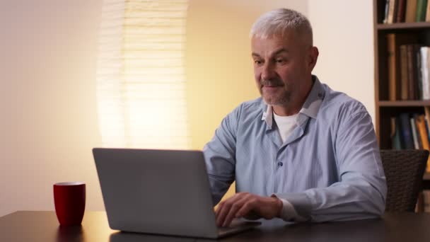 Homem idoso emocionalmente torcendo por sua equipe favorita assistindo jogo de esportes on-line no laptop em casa, câmera lenta — Vídeo de Stock