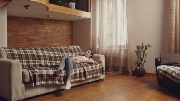 Молода вагітна жінка, що прокидається від денного сонця, стоїть з дивана і йде, відпочиває вдома — стокове відео