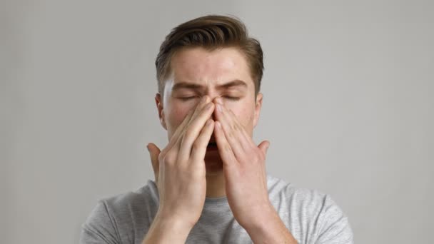 Close up portrait of young sick man rubbing his sore nose, grey studio background, slow motion — Stock Video