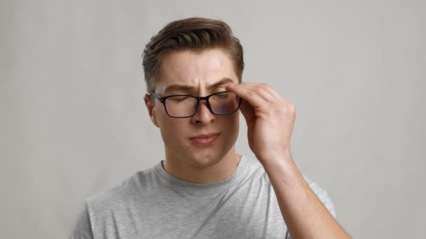 Jeune homme fatigué enlever ses lunettes et frotter ses yeux, fond de studio gris, ralenti — Video