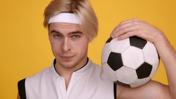 Close-up portret van jonge man dragen uniform holding voetbal, poseren voor camera, oranje studio achtergrond — Stockvideo