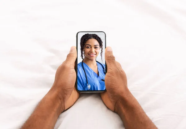 Männliche Hände halten Smartphone mit lächelndem Porträt schwarzer Ärztin auf dem Bildschirm — Stockfoto