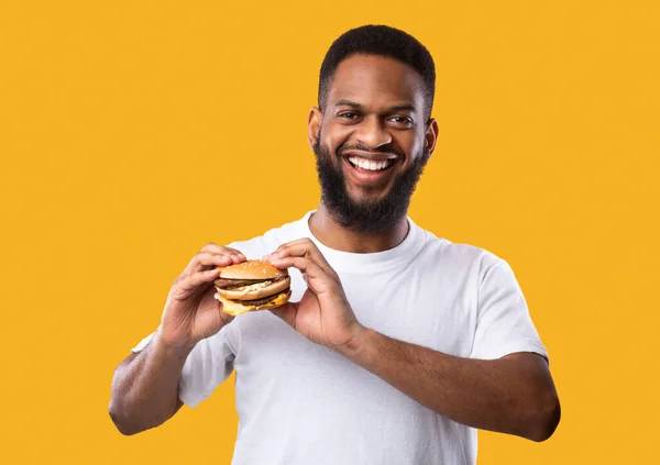 Homem negro posando segurando hambúrguer sorrindo para a câmera, tiro estúdio — Fotografia de Stock